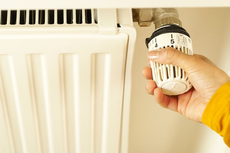 Main réglant la tête thermostatique d'un radiateur